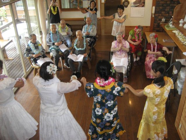 活動中のリビング空間 イベント 色鮮やかな衣装を身にまとったスタッフが、座っている方々と一緒に楽しげな催しを行っています。このような温かみのある雰囲気は、働く上での大きな魅力です。