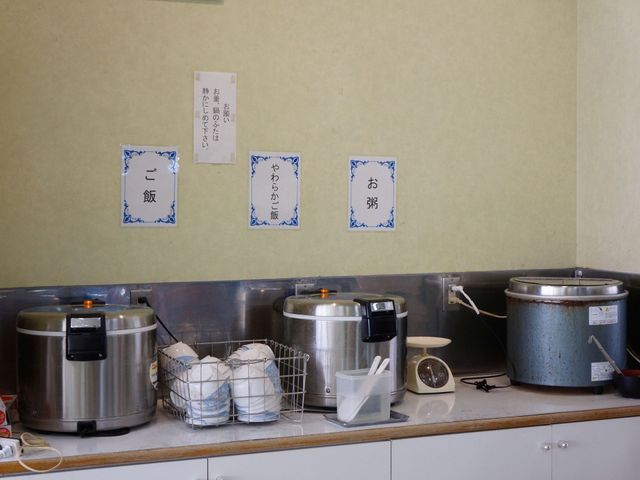 調理器具並ぶキッチンカウンター 食事 清潔なキッチンでは、毎日の美味しい食事をサポートするための様々な調理器具が整っています。ごはん釜やしきたりに合わせた食器も準備され、安心の食事環境が提供されています。