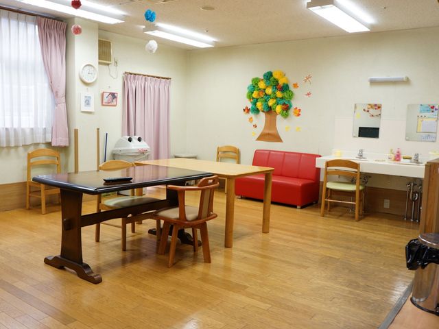 暖かみのある共有スペース 談話室 広々として明るい休憩所を備え、壁には季節感のある装飾が施されています。ベンチなどの座席があり、ゆったりとしたひとときを過ごせる空間です。