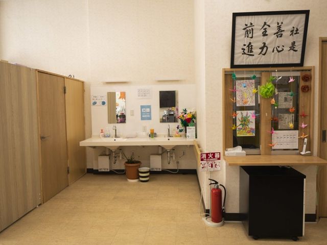 明るい洗面台のある廊下 廊下   木目調の収納と洗面台が並ぶ、すっきりした廊下です。掲示物や飾りもあり、職員が使いやすい工夫が見られます。