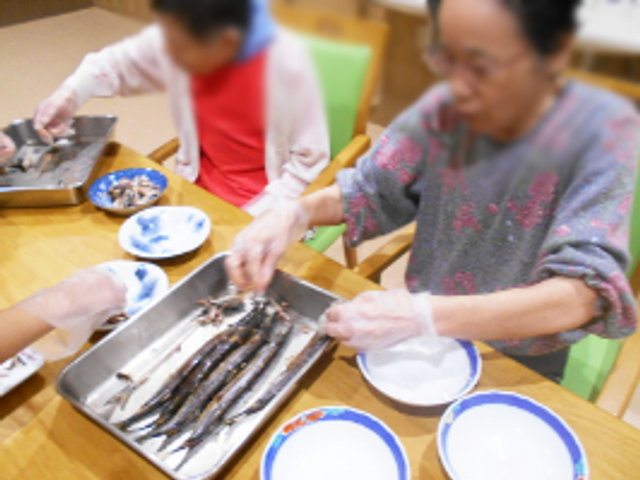 魚料理を準備する様子 ダイニングルーム 入居者が一緒に魚を手際よく調理しています。共同作業の場として活気があります。