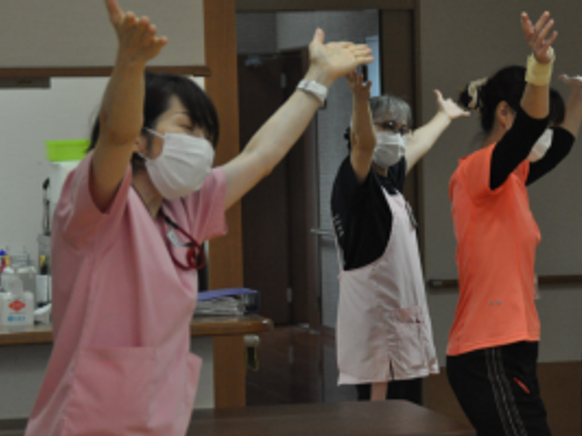 活動的なリビング 多目的室 笑顔で身体を動かす方々です。健康維持のための取り組みに、皆さんが楽しんでいらっしゃる様子が伝わります。