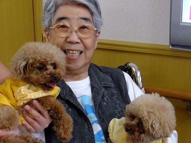 笑顔の女性と二匹の犬 イベント 愛くるしいペットと触れ合うスタッフの姿が、温かみのある雰囲気を感じさせます。利用者さまの日常に癒しを提供しています。