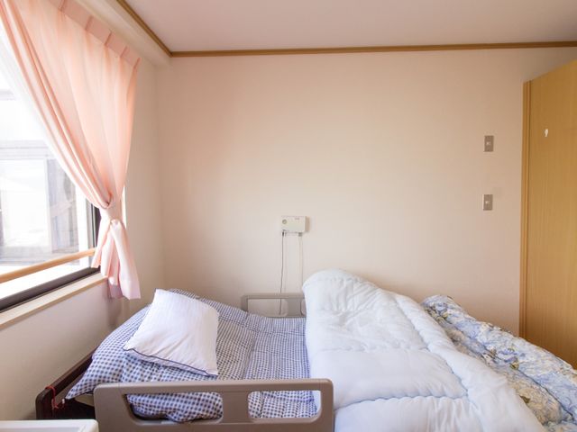 居室のシンプルなベッド 居室 採光を活かした居室で、日々の暮らしに安心と快適さを提供します。窓辺に優しい光が差し込み、穏やかな時間が流れています。