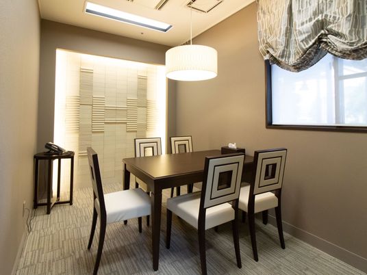 モノトーンで統一された個室に、テーブルと椅子5脚が据えてある。奧の壁面には間接照明が施されており、左側に電話が置かれている。