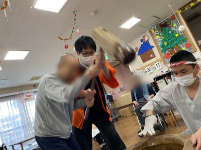 年末イベントで職員が杵を持って餅つきをサポートしている様子