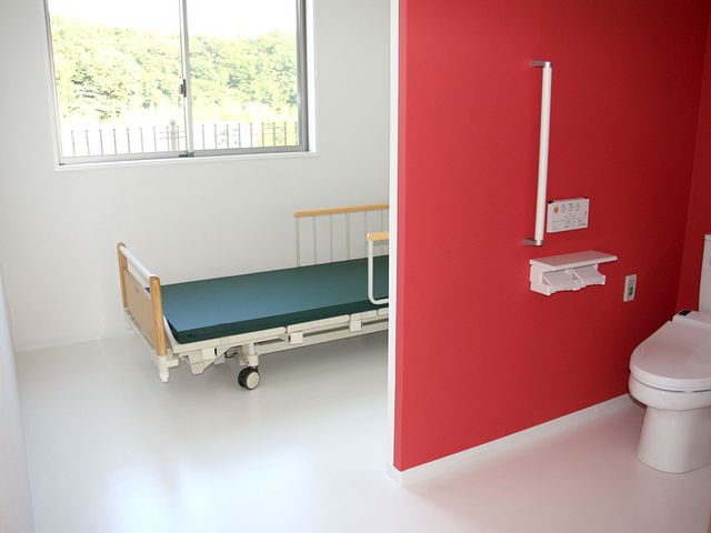 ベッドとトイレの居室 居室   部屋には、自然光が差し込む窓の近くにベッドが配置されています。明るい色調で落ち着いた雰囲気を提供しています。