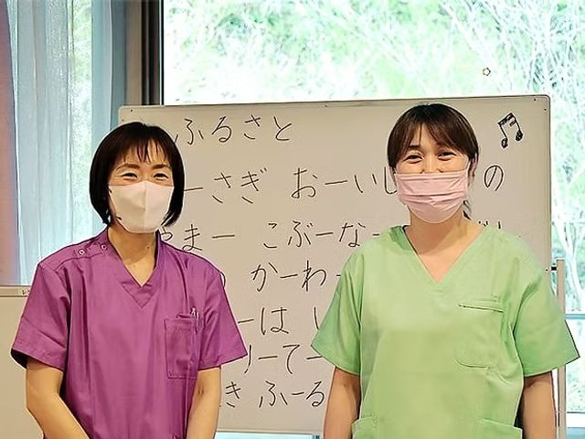スタッフが立つ明るい室内 多目的室   白板の前で、2人のスタッフが並んで立っています。窓から自然光が入り、やわらかな雰囲気の空間です。