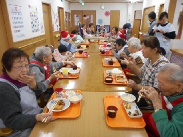 食事する人々の食堂 クリスマス会 温かい雰囲気の食堂で、多くの方が食事を楽しんでいます。明るい表情で会話を交わしながら、栄養バランスを考えた食事を提供しています。