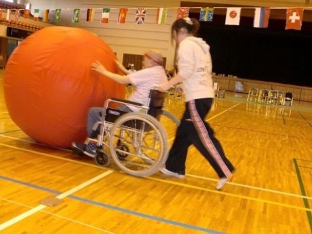 活動的な機能訓練の様子 運動会 車椅子の方が楽しそうに大きなボールと触れ合っており、周りの支援も手厚い安心な空間です。お仕事を通じてご利用者の健康支援ができます。
