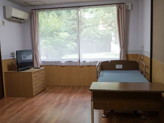 居室のベッドとテレビ 居室 窓辺に配されたベッドは明るく、落ち着いた時間を過ごせそうです。勤務先として、居心地の良さを感じられる空間です。
