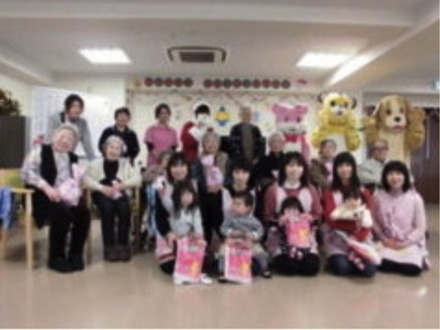 集合する人々の様子 記念写真 集い笑顔あふれる明るいスペースで、利用者様同士が交流を深め、楽しいひとときを過ごされています。スタッフと利用者の絆も感じられる空間です。