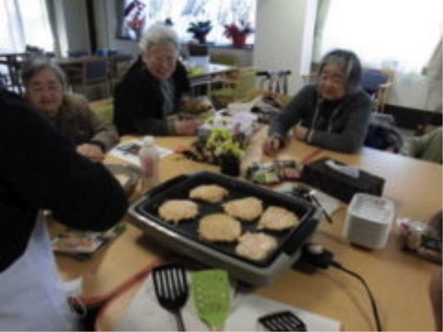 共有ダイニングでの料理 調理風景 共有スペースで提供される料理を楽しむ方々の笑顔が印象的です。温かな雰囲気の中で、共に食事をする時間が充実しています。