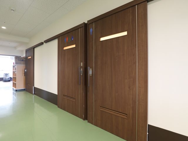 木製のトイレの扉 廊下 手を洗う場所が示された木の扉は、どなたでもお使いいただきやすいデザインです。清潔感があり安心してご利用頂ける環境が整っています。