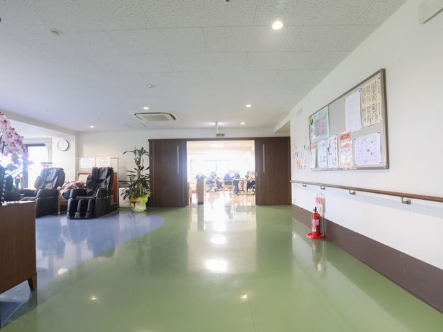 通路から見た明るい空間 廊下 ゆったりした椅子が並ぶ休憩スペースを抜けると、開放的なダイニングエリアが広がっており、明るい採光が心地よい環境を演出しています。