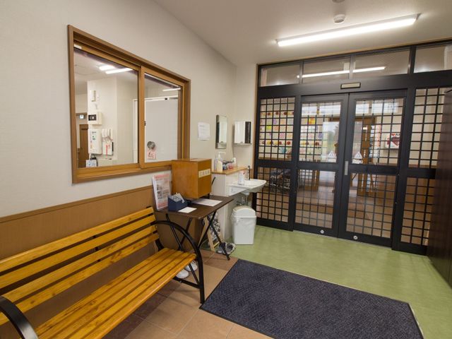 木の長椅子が置かれたエントランス 風除室 落ち着いた雰囲気のエントランスは、来訪者を暖かく迎える設計になっており、待合のためのベンチも設置されています。