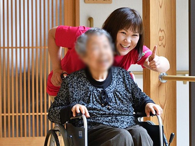笑顔のスタッフと車椅子の女性の廊下 廊下   笑顔のスタッフが、車椅子の女性と廊下を進んでいます。和やかな雰囲気で、温かい対応が感じられます。