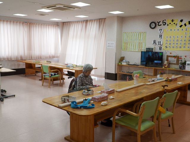多目的スペースの様子 食堂 ゆったりとしたスペースのある生活の場です。椅子に座った一人の方が、何かに集中している様子が見て取れます。