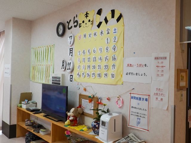 時計とカレンダーのある壁面 居間 様々な情報が掲示された壁と時計、心地よい雰囲気のあるスペースです。ここで休憩をとりながら、静かな時間を過ごすことができます。
