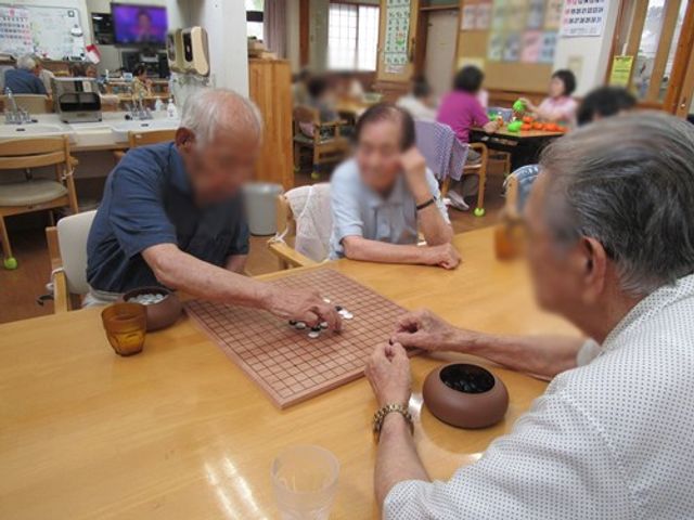 ゲームを楽しむ人々テーブル 多目的室 落ち着いた雰囲気の中で、入居者同士が卓上ゲームを楽しんでいます。交流が広がる空間です。