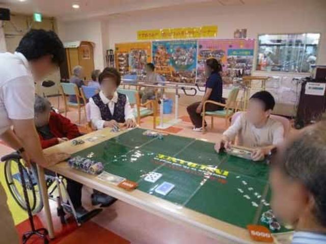 多世代が交流する共有スペース イベント 利用者が和気あいあいとゲームを楽しんでおり、スタッフも笑顔で支援しています。この場所では、さまざまな活動を通じてコミュニケーションが図れます。
