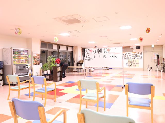 多目的利用可能な広間 共有スペース カラフルな椅子が配置され、明るく広々とした空間です。自動販売機や掲示物があり、様々な活動が行われる場所です。