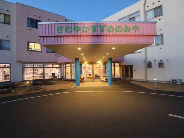 夕暮れ時の施設エントランス 外観 広々として明るい入口は、ご自由に出入りしやすいよう配慮されています。夕暮れ時も建物は明るく、安心感を与えるような雰囲気が漂っています。