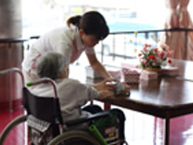車椅子の利用者とスタッフ ラウンジ 車椅子の利用者が、スタッフとテーブルで一緒に時間を過ごしています。温かい雰囲気が漂っています。