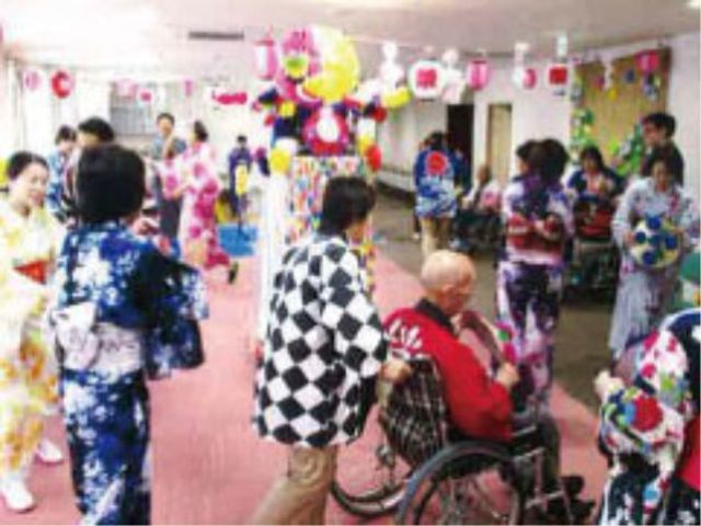 お祭り気分の多目的室 イベント行事 着物を着た方々が楽しいひとときを過ごしており、車椅子の方も交えて笑顔で賑わっています。ここは、共に喜びを分かち合える温かい空間です。