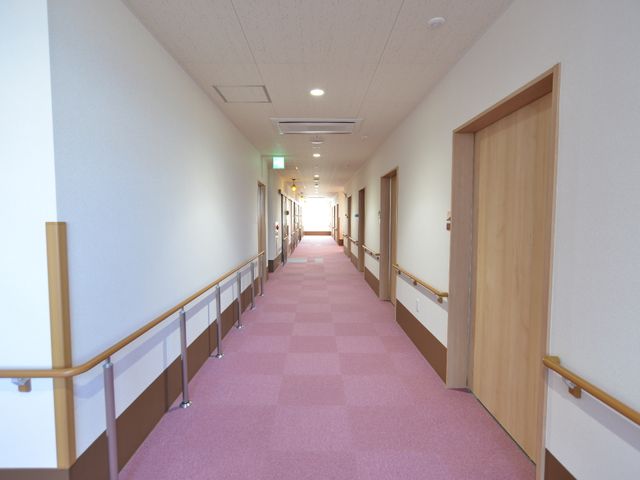 明るく清潔な廊下 利用者への配慮をした廊下 手すりが設置された落ち着いた色合いの廊下です。行き交うスタッフや利用者の方々が快適にお過ごしいただける設計となっています。