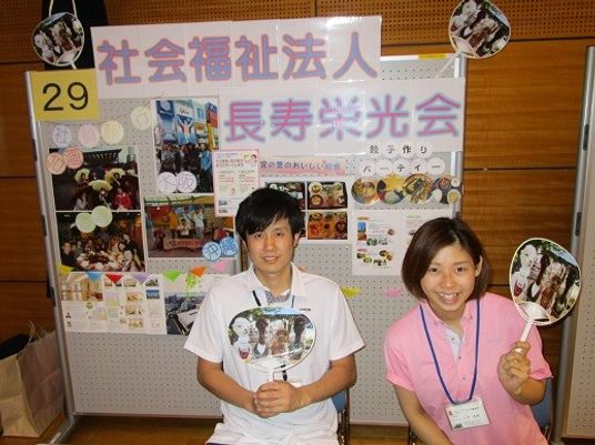 スタッフの案内掲示前で笑顔の2人と掲示物  