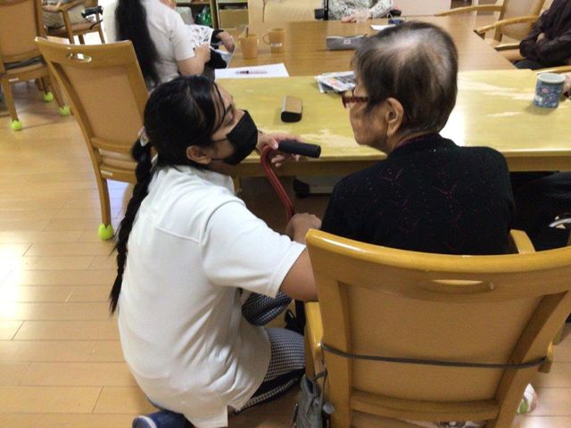 介護スタッフと利用者の対話 共有スペース ケアするスタッフが優しく利用者の話に耳を傾けており、和やかな雰囲気の居室が広がっています。