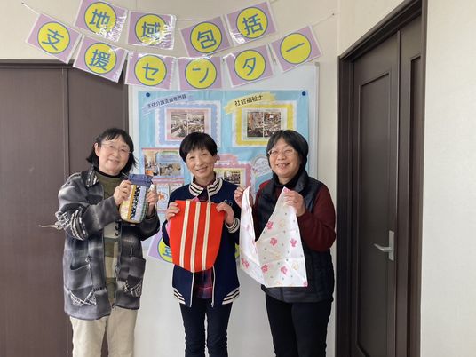 地域包括支援センターの掲示前で3人が並ぶ様子  