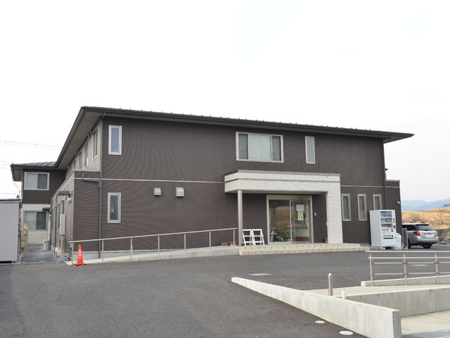 茶色い建物の外観 外観 キレイに整備された外観の建物です。広々とした駐車場が設けられ、入り口に自動販売機も見受けられます。