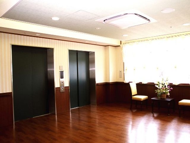 明るい広いロビー エレベーターホール ゆったりとした空間には暖かい色合いの床や壁が印象的です。待合や休憩に最適な椅子も設置され、訪れる人に安らぎを提供しています。