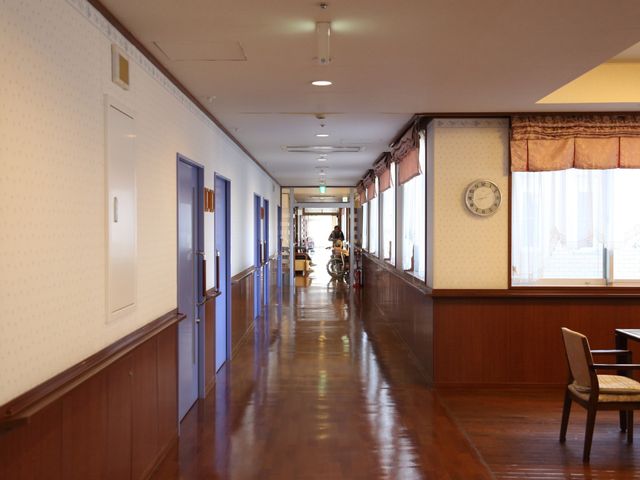 清潔な廊下とスタッフ 通路 ゆったりとした廊下は静かで、温かみのある照明が印象的です。スタッフが入居者のサポートをしており、心地よい環境が感じられます。