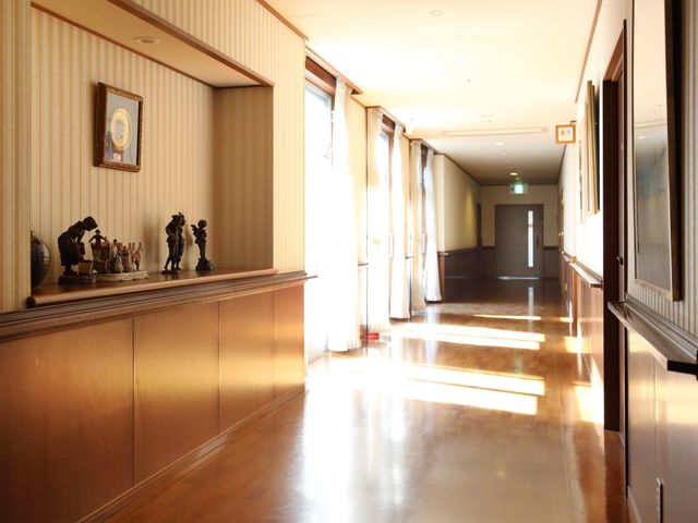 木目調の温かみのある廊下 通路 日差しが差し込む落ち着いた雰囲気の廊下です。壁には飾り棚とアートがあり、訪れる方に安らぎを提供しています。