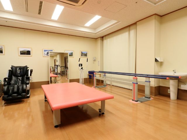 リハビリ設備の整った室内 機能訓練室 広々とした機能訓練室は、明るい光が差し込み、リハビリに必要な設備が整っています。サポートが必要な方々の生活向上に役立っています。