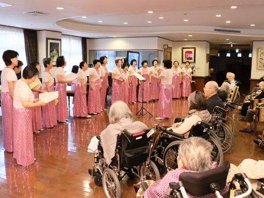 おそろいのピンクのロングドレスと白いショールを身につけた女声合唱団によるコンサート。