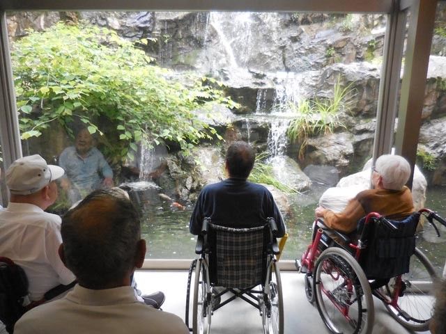 四人が滝を眺める壁面 庭 大きな窓から、小滝が見える場所です。自然の風景を眺めながら、リラックスできる空間です。