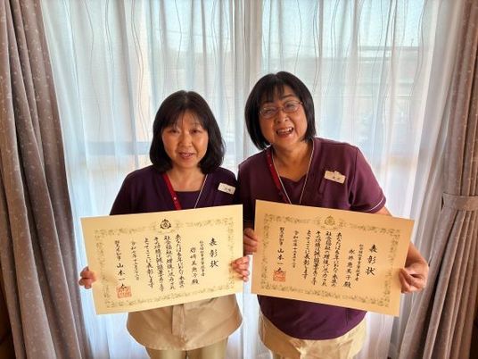 賞状を持つ職員2人の室内