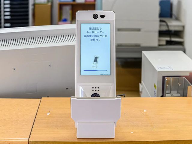 顔認証端末の受付 フロント   顔認証付きカードリーダーが置かれた受付です。来訪者の確認をスムーズに行いやすい環境がうかがえます。
