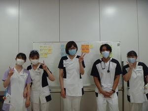 スタッフ5人が並ぶ掲示板前  