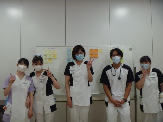 スタッフ5人が並ぶ掲示板前  