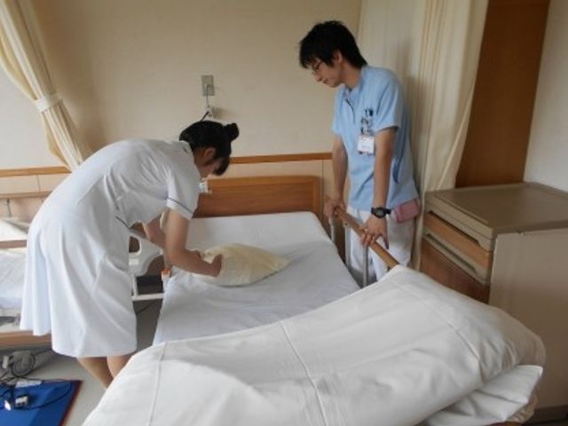 居室でベッドを整える職員 居室   職員がベッドメイキングをしている居室です。明るく整った空間で、日々の支援の様子が伝わります。