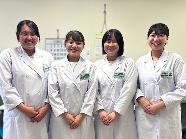 白衣のスタッフが並ぶ休憩室 休憩室   白衣のスタッフ4人が笑顔で並んでいます。明るい室内で、働く人の雰囲気が伝わります。