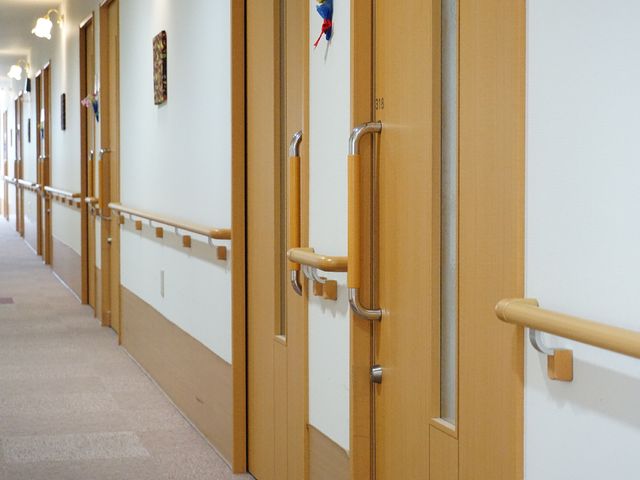 廊下の手すりと部屋の扉 廊下 手すり付きの広々とした廊下は安全に配慮され、まるで家のような温かみを感じさせます。扉には番号があり、整然と並んでいます。