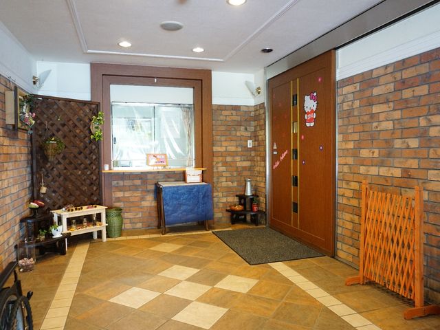 エントランスの温かみある風景 玄関 レンガ造りの壁が温もりを感じさせるエントランスです。明るい色合いと装飾が、訪れる方々を優しく迎え入れます。