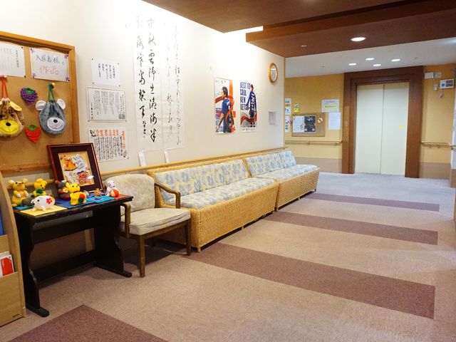 温もりある待合スペース 廊下 座り心地の良いソファが並び、壁には和風の装飾や掲示物が飾られており、落ち着いた雰囲気の待合スペースが広がっています。ゆったりとした時間をお過ごしいただける環境を備えています。