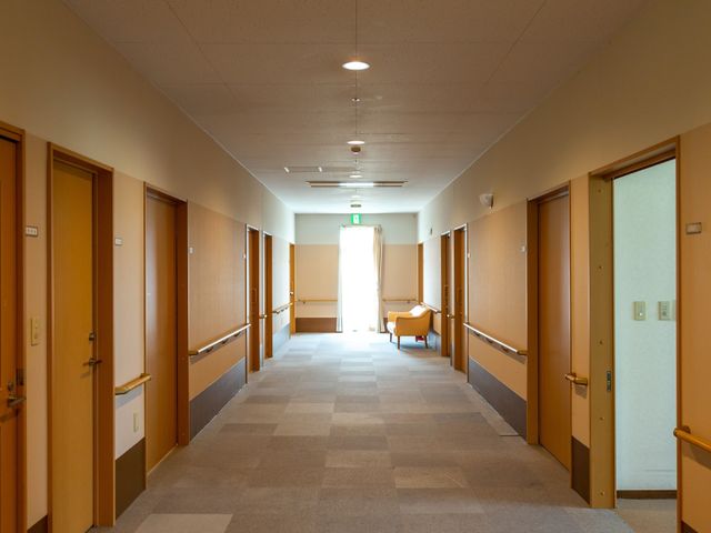 廊下の明るく広々とした空間 廊下 ゆったりとした通路には落ち着いた色合いの扉が並び、心地よい安堵感を与えてくれます。通りに面して配置された椅子では、ひとときのくつろぎが得られそうです。